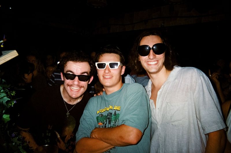 three college men wearing sunglasses and smiling at a party at night