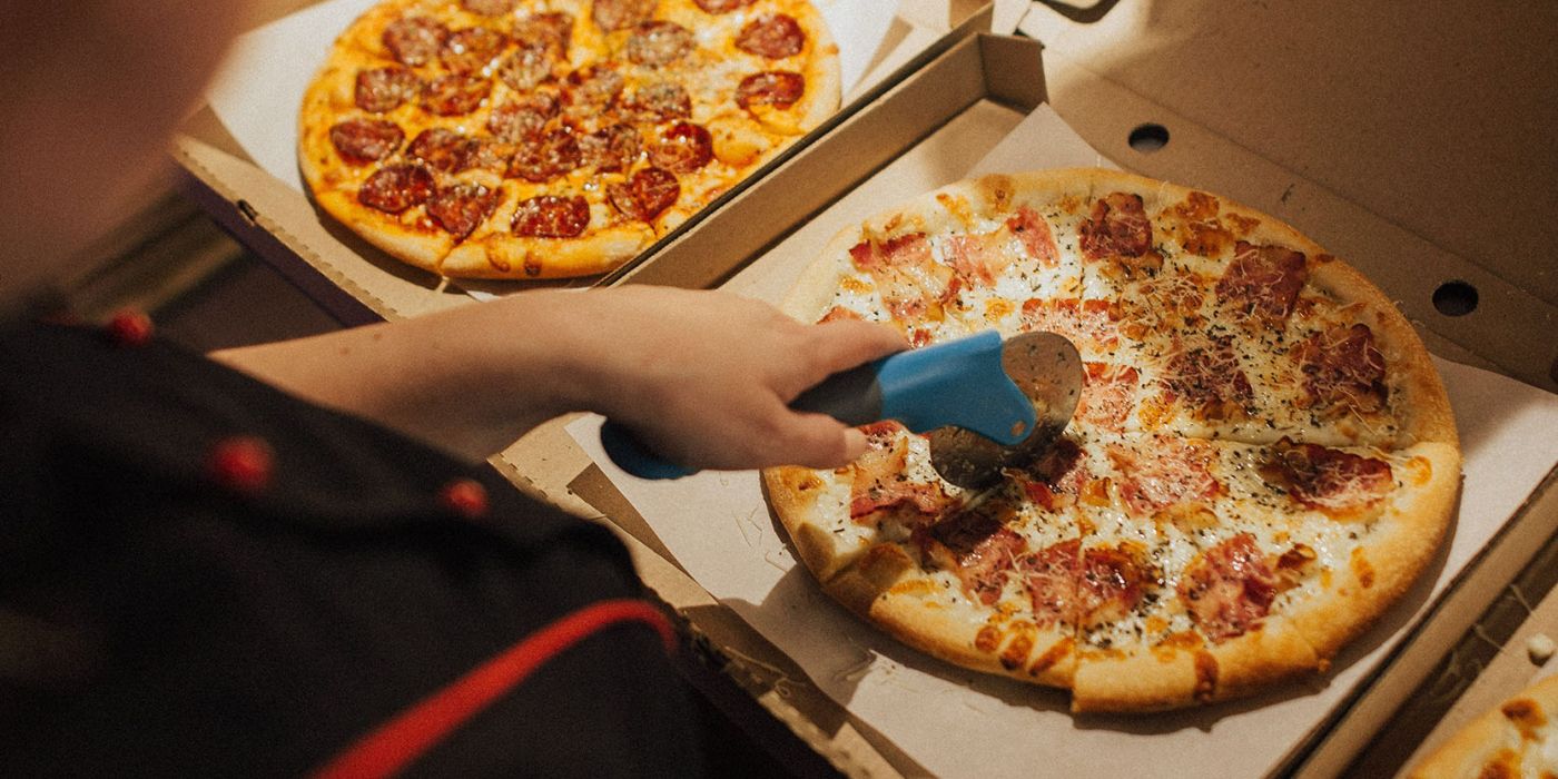 persona cortando una pizza con un cortador de pizza