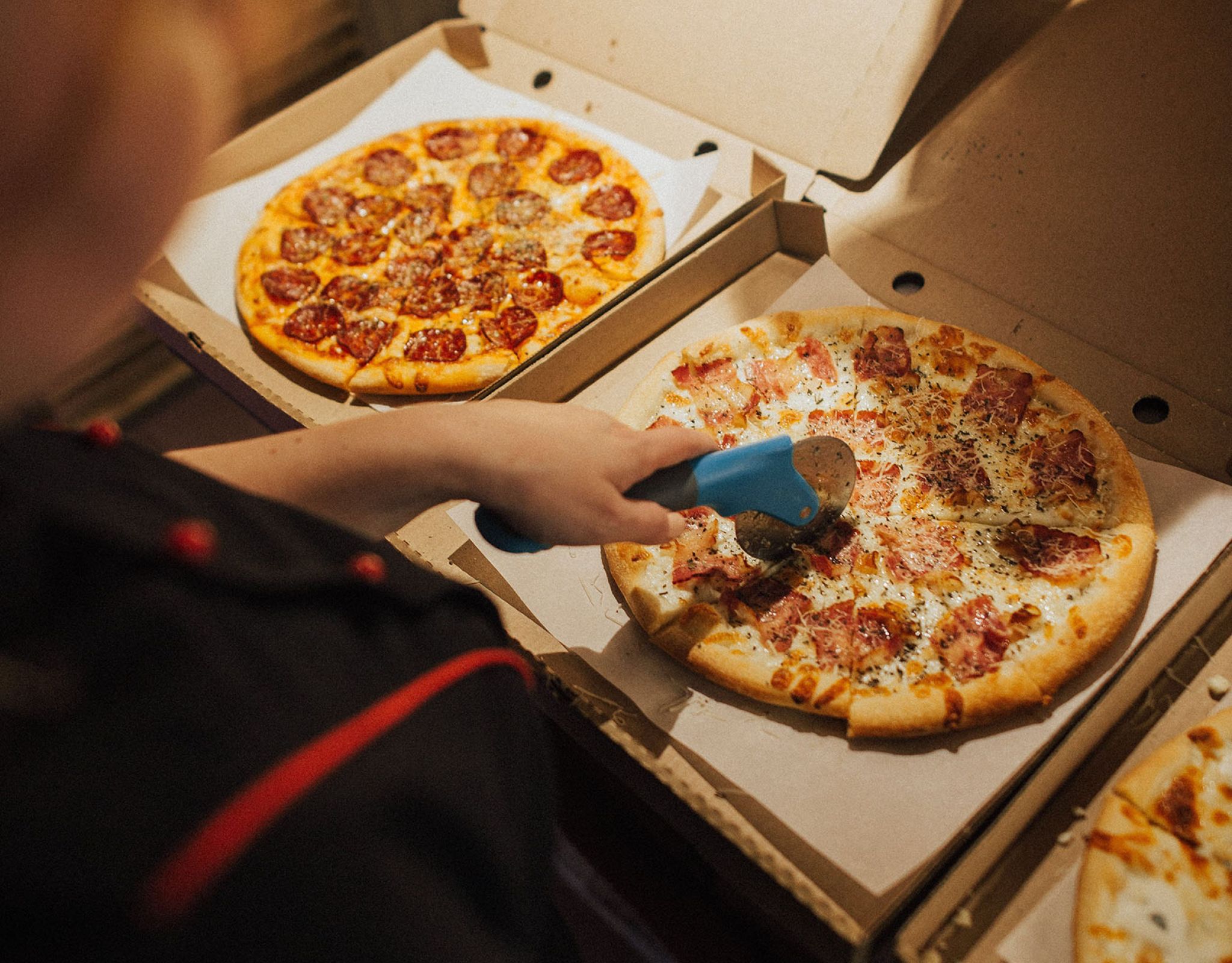 person cutting a pizza with a pizza cutter